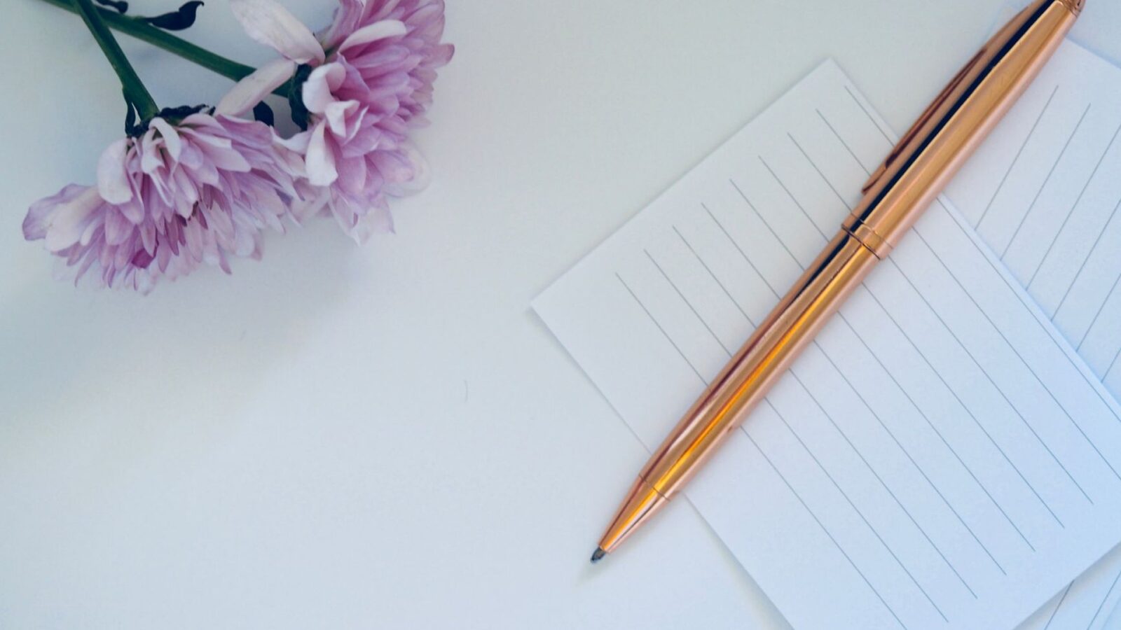 Goldener Stift auf leeren Karten neben Blumen als Vorlage für Sprüche zur Silberhochzeit